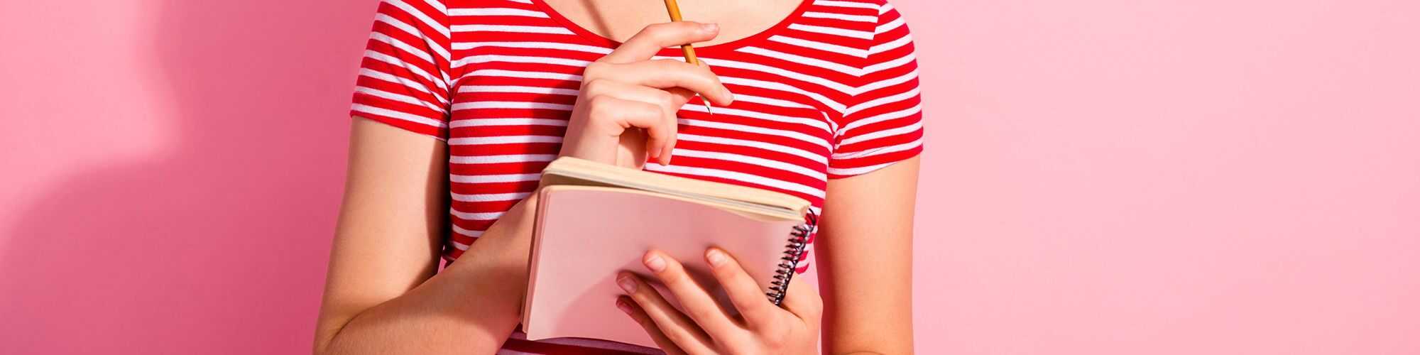 Torse de femme, sur fond rose. Elle a un cahier et un crayon qu'elle ramène à sa bouche en signe d'interrogation.
