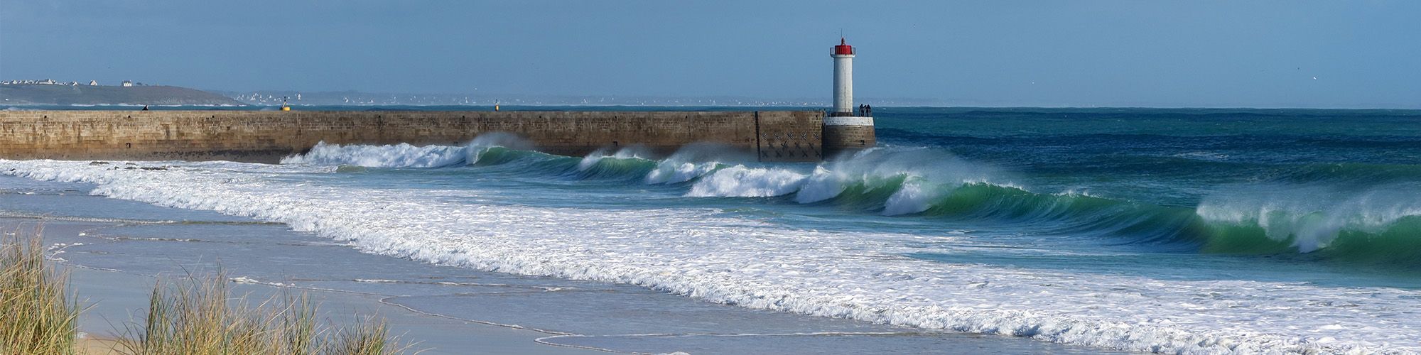 Le môle et le feu du Raoulic, en contrebas on voit une vague et de l'écume sur la plage