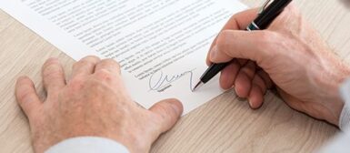 Deux mains en gros plan, la main droite tient un crayon et signe un document papier poser sur le bureau.