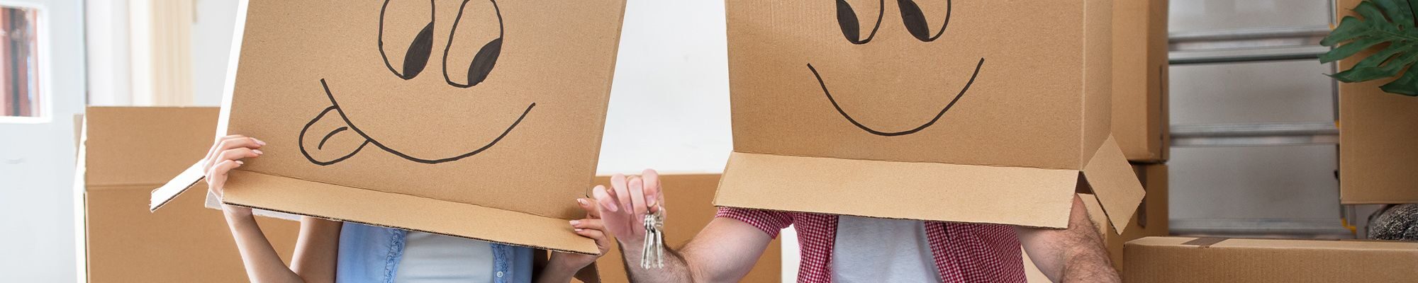 Une femme et un homme assis en tailleur dans une pièce avec des cartons, les deux personnes ont un carton sur la tête avec un dessin de visage souriant dessus.
