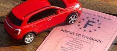 Un permis de conduire et une figurine de voiture rouge posés sur une table en bois.