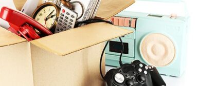 Image de carton rempli de divers objet, une horloge, un téléphone rouge, une télécommande. Sur le côté il y a poste radio bleu, et une manette de console noire.
