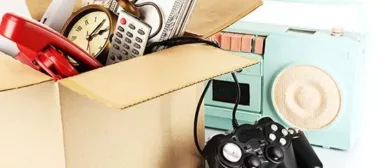 Image de carton rempli de divers objet, une horloge, un téléphone rouge, une télécommande. Sur le côté il y a poste radio bleu, et une manette de console noire.