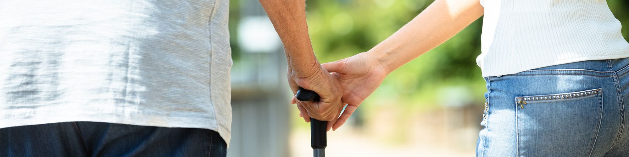 Une personne âgée qui marche avec une cane, une femme l'aide pour se déplacer.