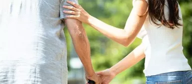 Une personne âgée qui marche avec une cane, une femme l'aide pour se déplacer.