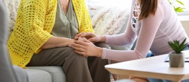 Une femme âgés qui est aidée par une aide à domicile qui lui tient la main.