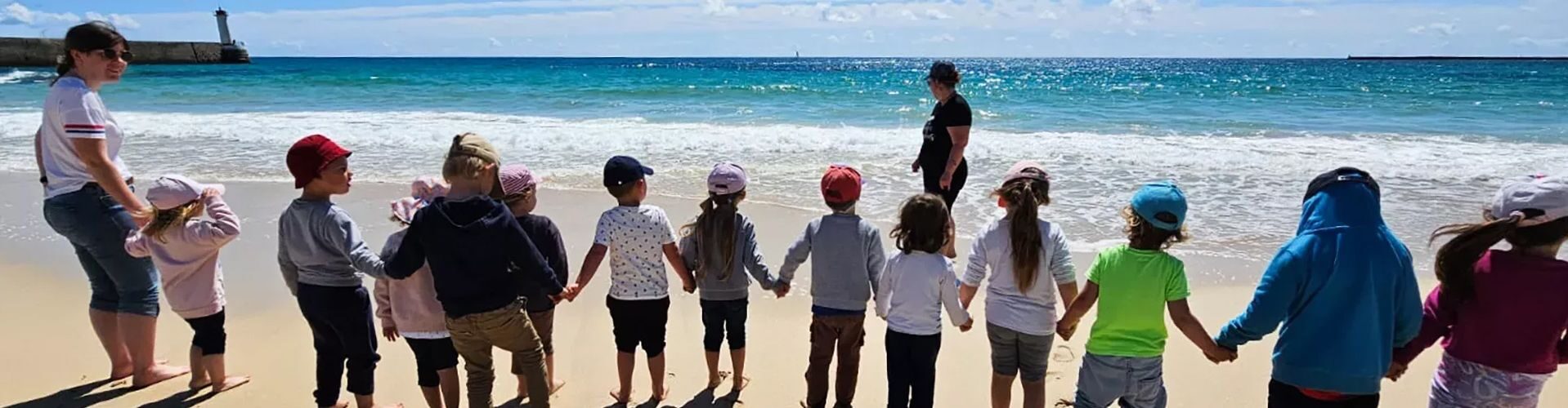 Un groupe d'enfant qui se tiennent la main sur la plage de Trescadec, encadrés par deux adultes.