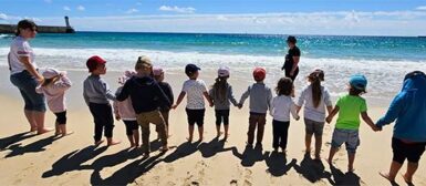 Un groupe d'enfant qui se tiennent la main sur la plage de Trescadec, encadrés par deux adultes.