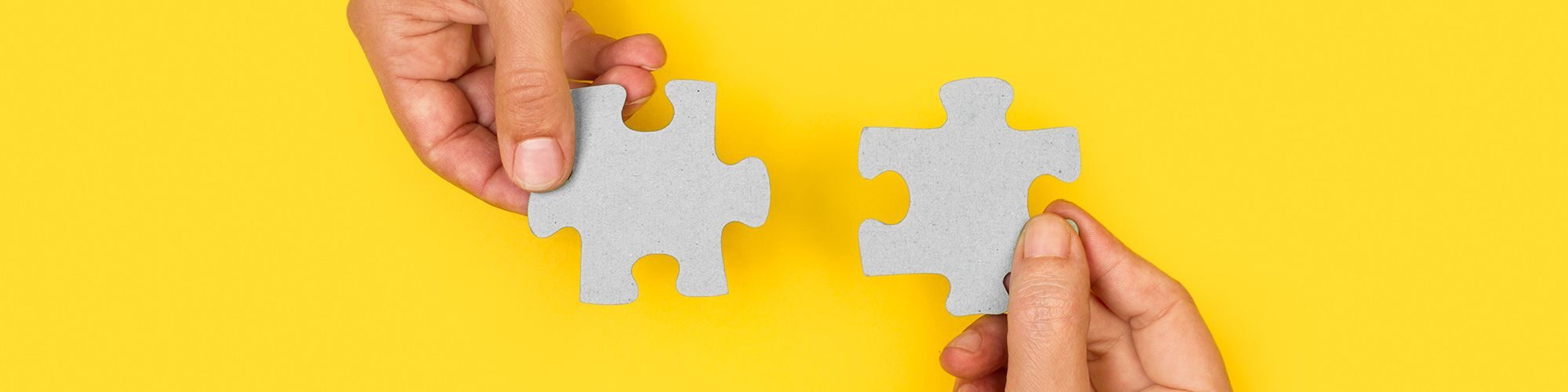 Deux main avec des pièces de puzzle, sur fond jaune.