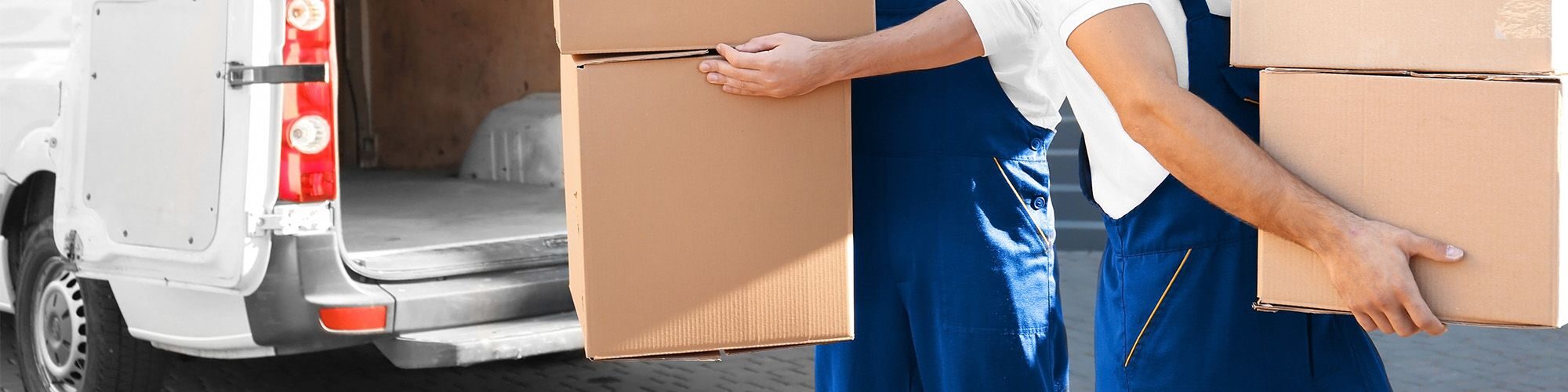 Deux déménageurs en chemise blanche et salopette bleue, qui portent chacun deux cartons, dans un camion blanc.