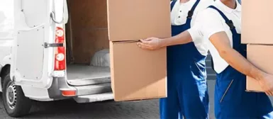 Deux déménageurs en chemise blanche et salopette bleue, qui portent chacun deux cartons, dans un camion blanc.