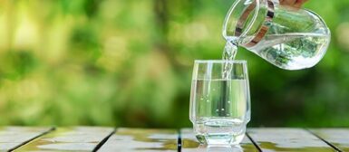 Quelqu'un qui verse de l'eau depuis une carafe dans un verre.