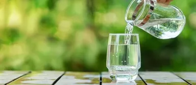 Quelqu'un qui verse de l'eau depuis une carafe dans un verre.