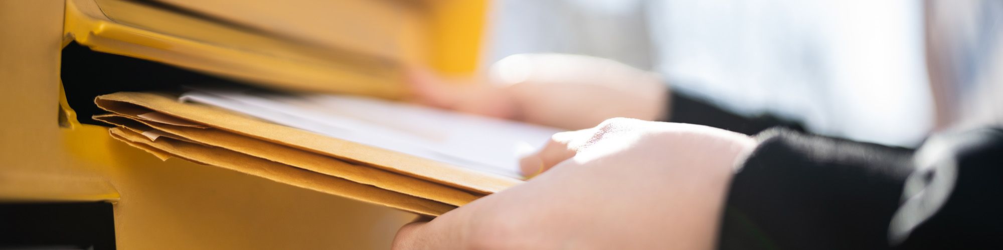 Gros plan sur les mains de quelqu'un qui poste des lettres dans une boîte aux lettres.