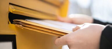 Gros plan sur les mains de quelqu'un qui poste des lettres dans une boîte aux lettres.