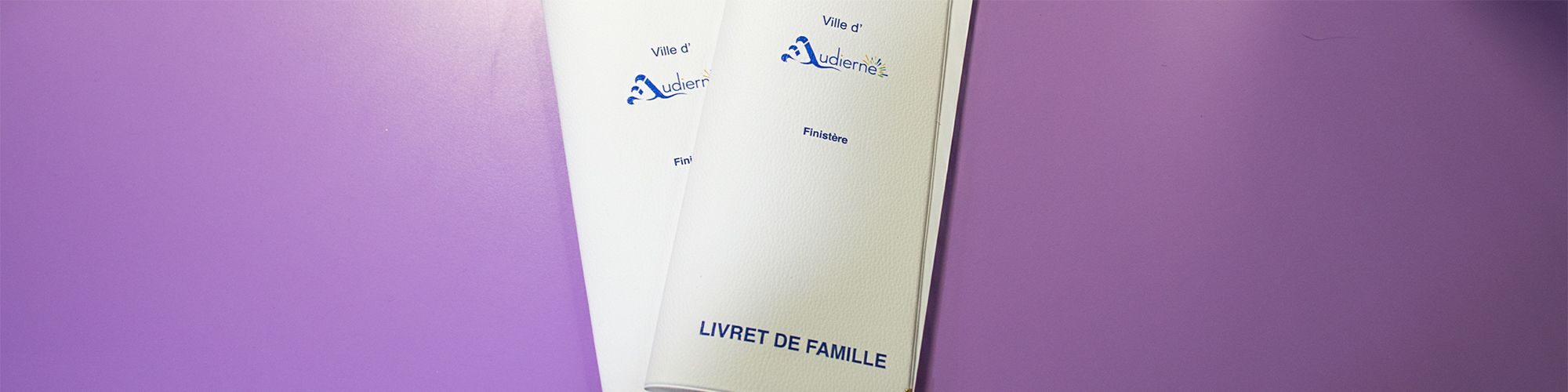 Deux livrets de famille, blancs avec le logo de la ville d'Audierne, et la mention Finistère. Les deux livrets sont superposés sur fond violet.