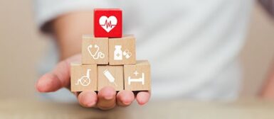 Une personne qui tient des blocks de bois sur lesquels figurent des dessins de stéthoscope, de médicament, de fauteuil roulant, de piqûre et un lit médicalisé.