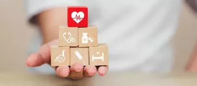 Une personne qui tient des blocks de bois sur lesquels figurent des dessins de stéthoscope, de médicament, de fauteuil roulant, de piqûre et un lit médicalisé.