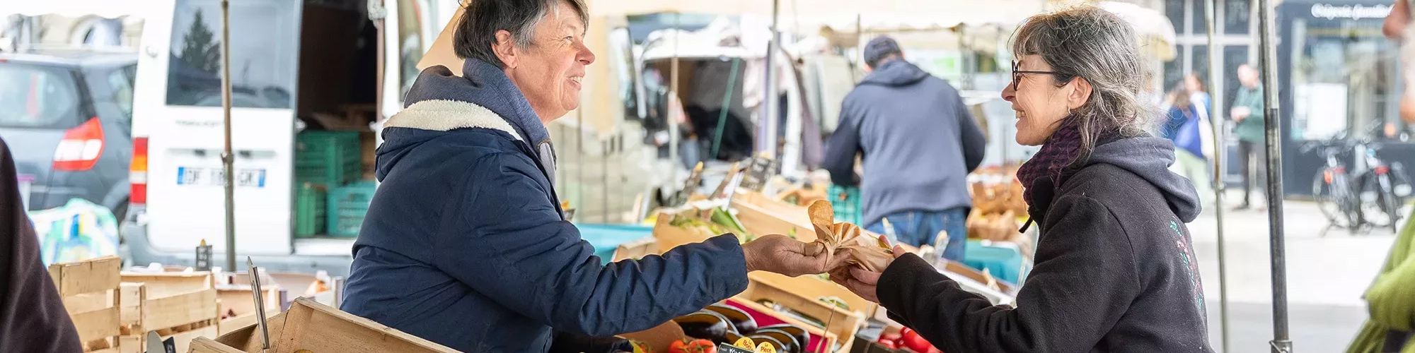 Image d'une maraîchère sur un marché qui vend ses produits à une cliente.