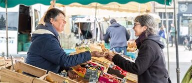 Image d'une maraîchère sur un marché qui vend ses produits à une cliente.