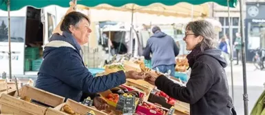 Image d'une maraîchère sur un marché qui vend ses produits à une cliente.