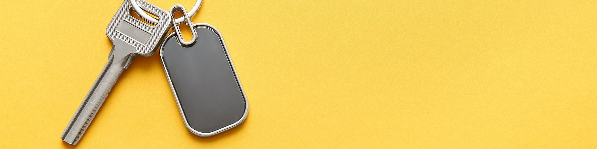 Une clé et un badge magnétique sur un porte-clés, sur fond jaune.