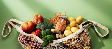 Un sac de courses qui déborde sur un fond vert. Dans le sac il y a des pommes, des tomates, des brocolis, des patates, des poids chiches, de la coriandre, etc