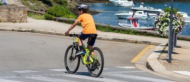 Un enfant qui roule à vélo sur la route, en arrière plan on peut voir le port et des bateaux.