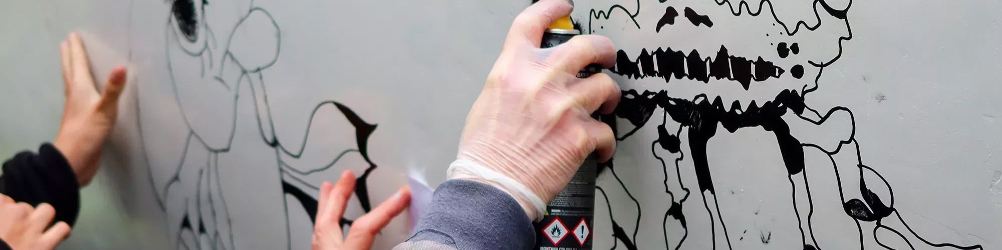 Zoom sur les mains de personnes qui font un graffiti avec des bombes de peintures.