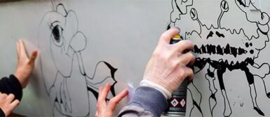Zoom sur les mains de personnes qui font un graffiti avec des bombes de peintures.
