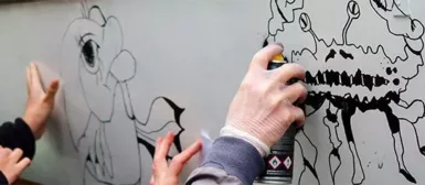 Zoom sur les mains de personnes qui font un graffiti avec des bombes de peintures.