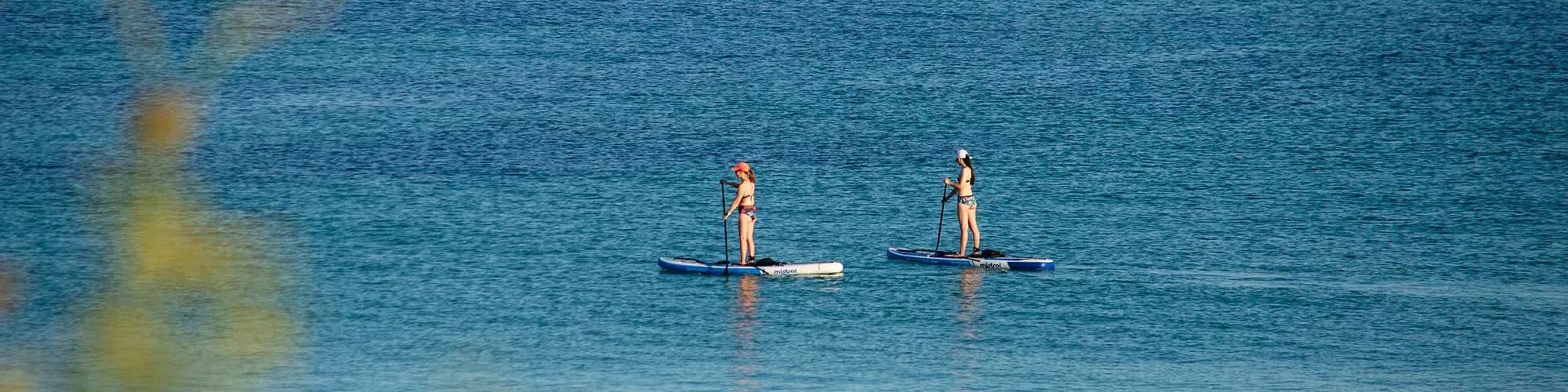 Deux femmes faisant du paddle sur une mer calme.