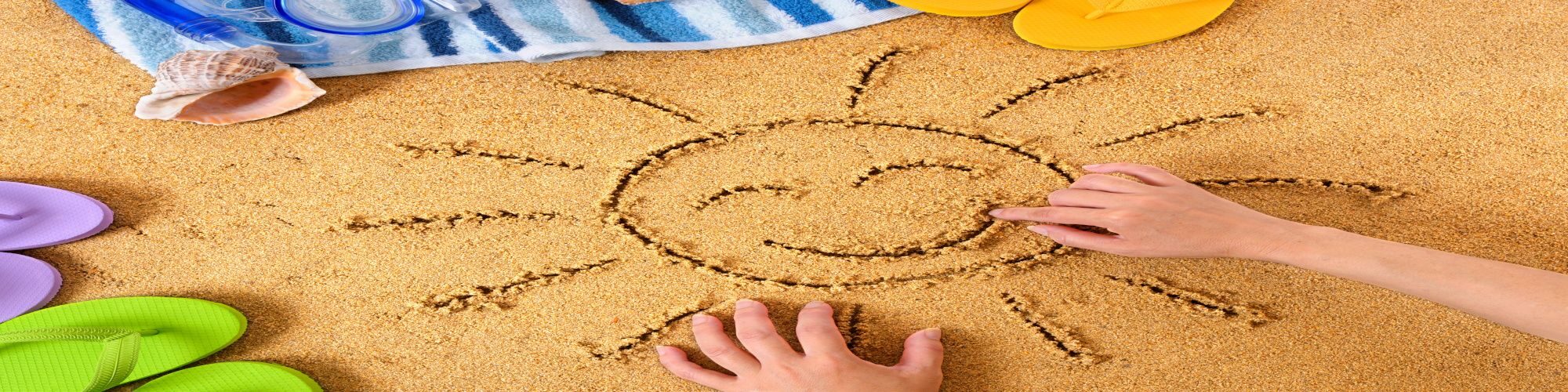 Un enfant qui trace un soleil qui sourit dans le sable.